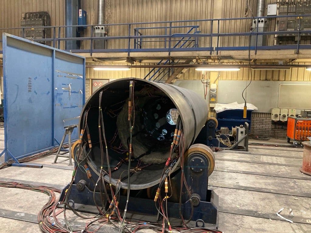 Large rolled steel cylinder on welding rotators in a fabrication shop