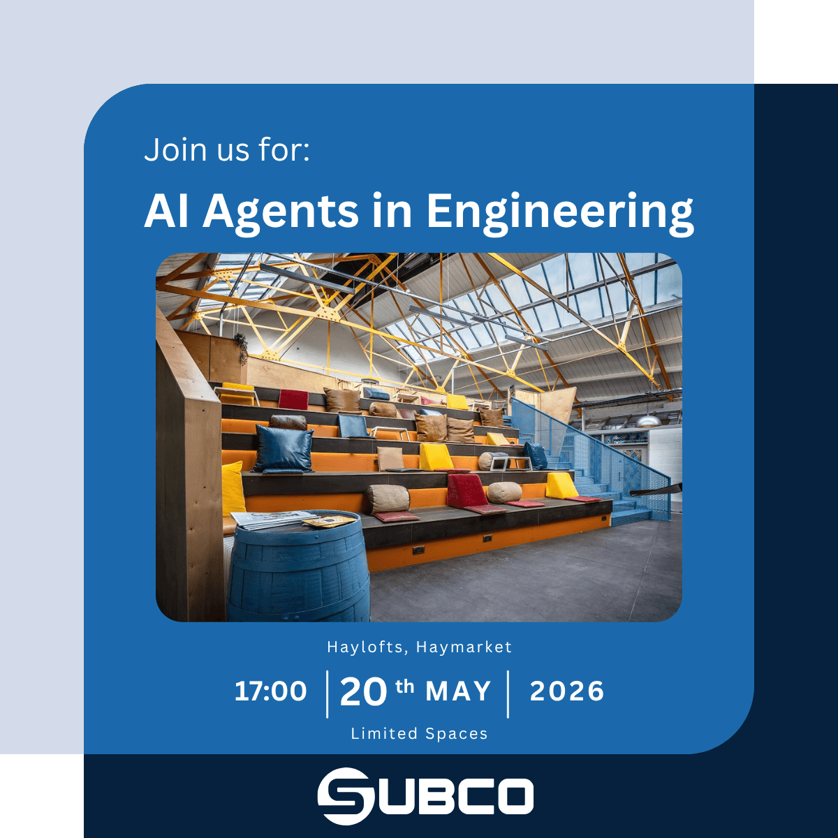 The auditorium space at The Haylofts, Newcastle. A bright, industrial event space featuring tiered wooden seating with orange backing, scattered with leather, fabric and felt cushions in red, yellow, blue, brown and tan. The ceiling is open and beamed with exposed yellow steel trusses and skylights overhead. A blue metal staircase runs up the right-hand side, and a blue wooden barrel stacked with magazines sits in the foreground. Located at Haylofts, 5 St Thomas Street, Newcastle, NE1 4LE.